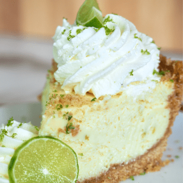 Award winning key lime pie recipe, slice on a plate topped with whipped cream and a lime.