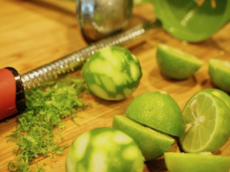 zesting limes with microplane on cutting board, cut limes and zested limes laying around.