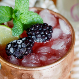 Blackberry Bourbon Mule square image with close up of copper mule cup frozen blackberries and an icy cold moscow mule.