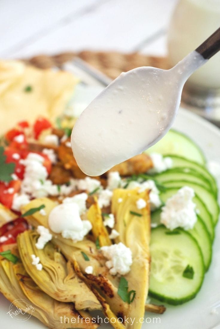 Spoonful of garlic lemon sauce going onto Grilled Chicken Shawarma bowl. 