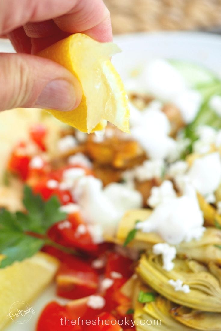 Squeezing a lemon onto  a bowl of grilled chicken shawarma. 