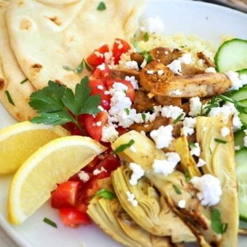 Shawarma chicken on a plate with fresh tomatoes, cucumbers, artichokes and lemons.