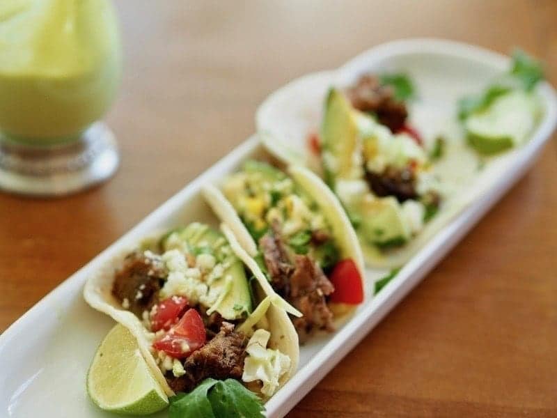 Mexican barbacoa beef street tacos with limes, avocados, tomatoes and cheese on a platter. 