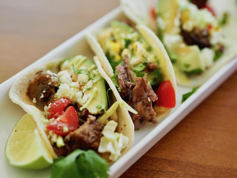 Close up of street tacos on ceramic plate with lime and cilantro. 