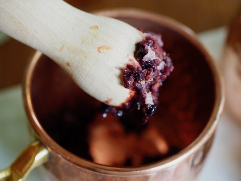 smashing blackberries with a muddler into a copper mug.
