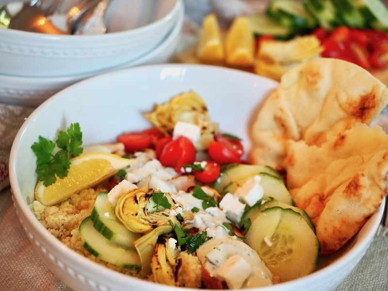 Chicken Shawarma Bowl in a bowl with couscous, cucmbers, tomtaoes, homemade naan and a lemon wedge. 