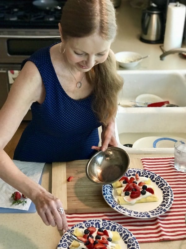 my friend Eliza, preparing crepes with creme and fresh berries near her kitchen sink. 