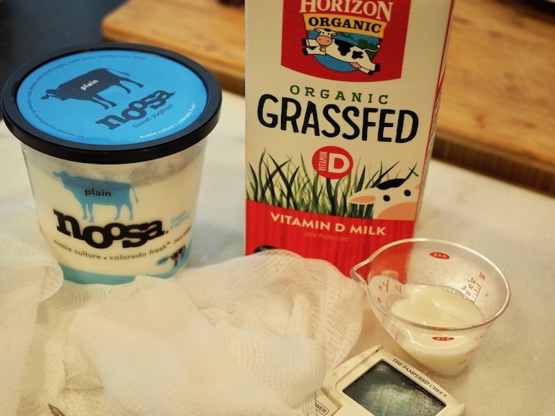 Container of Noosa plain yogurt, carton of organic milk, cheesecloth, timer and small measuring cup of plain yogurt | www.thefreshcooky.com