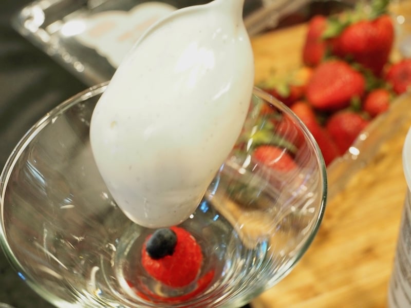 Shot of raspberry with blueberry in center with spoonful of vanilla yogurt going on top of berry.