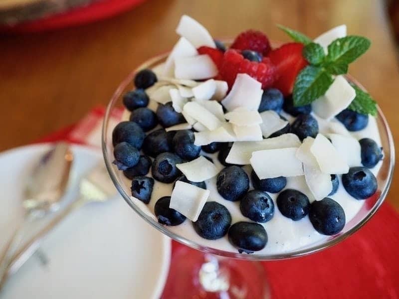 Finished red, white and blue yogurt parfait, with shaves of coconut, sprig of mint and blueberries on top.