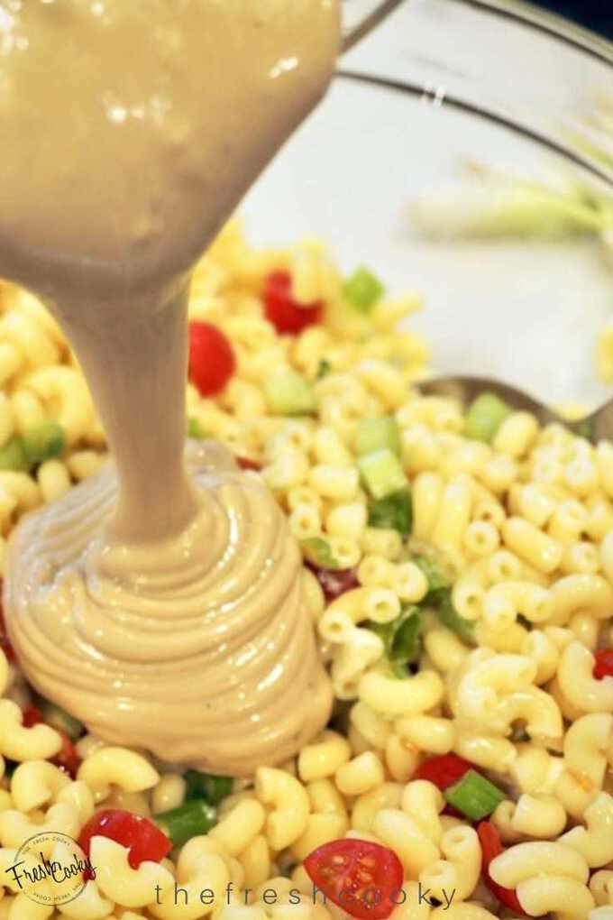 Pouring creamy balsamic ranch vinaigrette onto macaroni salad.