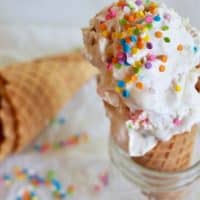 Circus Animal No Churn Ice cream with two scoops on a sugar cone sitting in a glass with sprinkles on top.