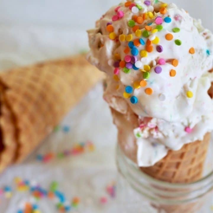 Circus Animal No Churn Ice cream with two scoops on a sugar cone sitting in a glass with sprinkles on top.