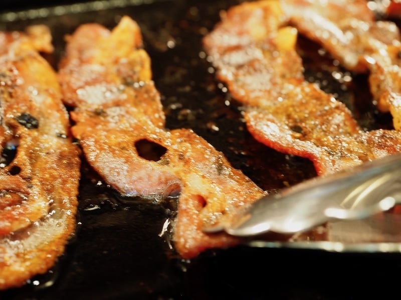 Frying up crisp bacon close up.