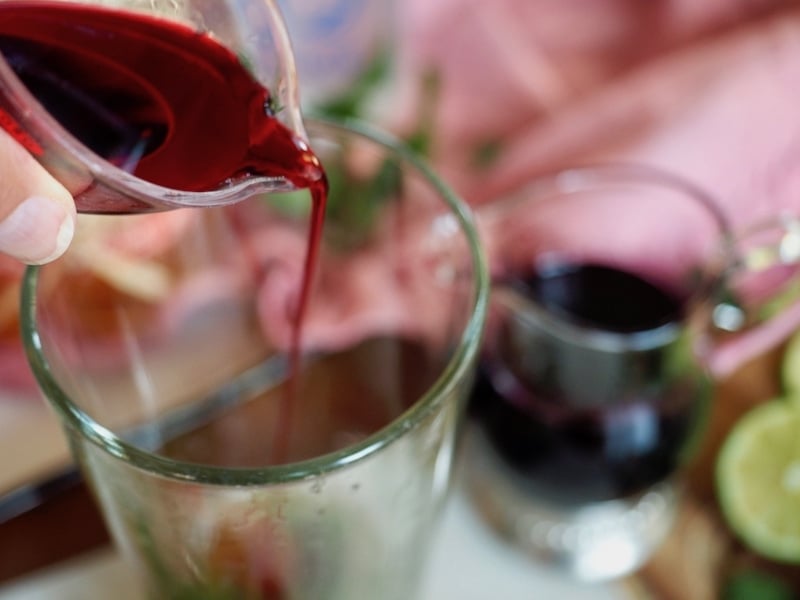 Pouring hibiscus simple syrup into tall glass using mini measuring cup.