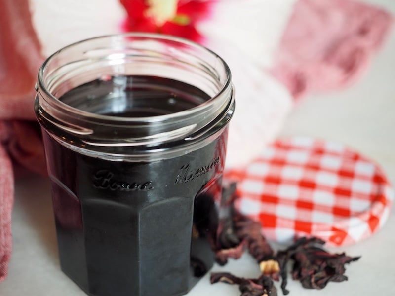 Small glass jar filled with simple syrup, with lidd and flower in background. 