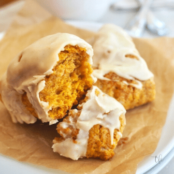Square image of Pumpkin Scones on a plate, one scone broken in half to reveal a tender, pumpkin spiced center.
