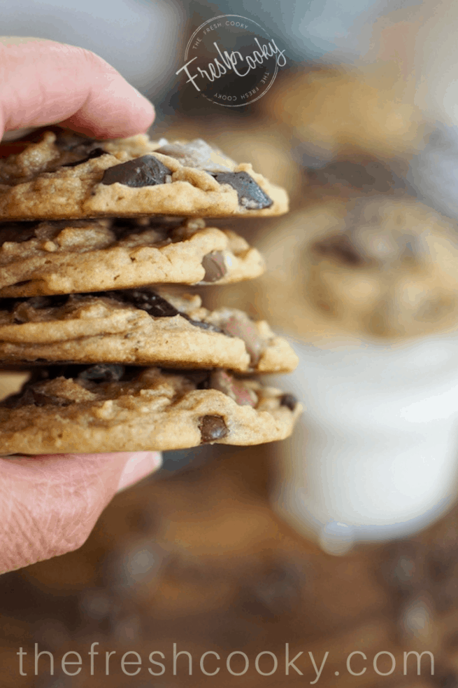 Hand holding 4 stacked triple chocolate chip cookies. 