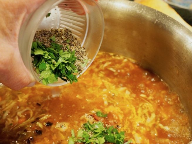 pouring in herbs and spices into bacon beef minestrone soup