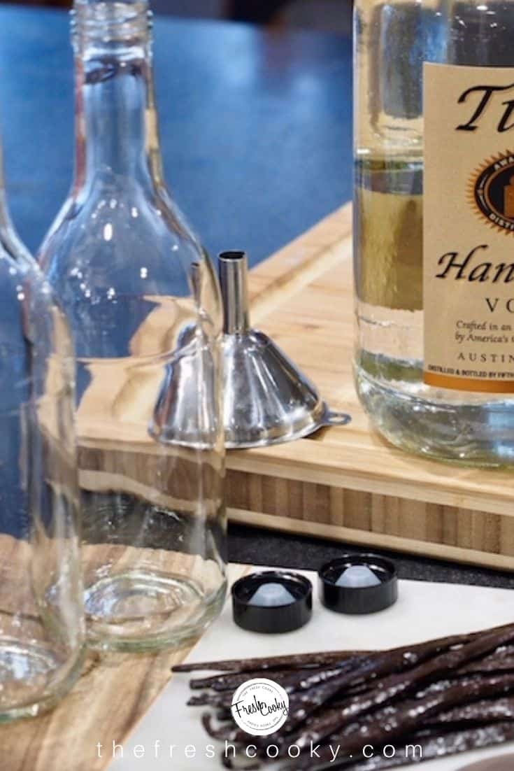 two empty glass beverage bottles with lids, a stainless steel funnel and bottle of Titos Vodka with fresh vanilla beans in foreground.