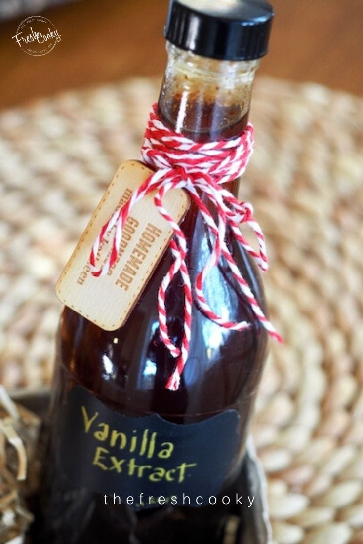 Bottle of vanilla extract with red and white bakers twine tied in bow sitting in a berry box with shreds around it. 