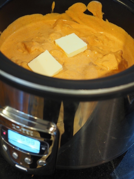 Pats of butter on top of crock pot full of butter chicken, ready to cook 