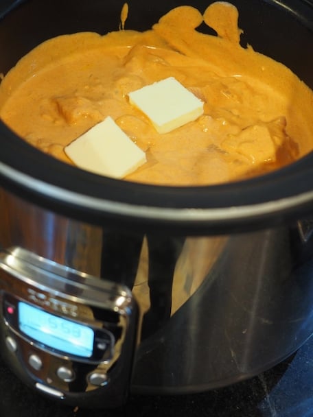 Pats of butter on top of crock pot full of butter chicken, ready to cook
