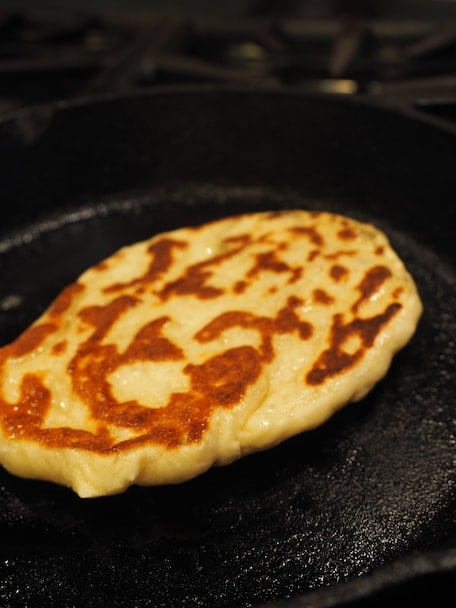 Golden naan bread in a hot skillet.
