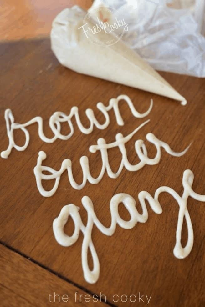 Piping bag filled with brown butter glaze laying on wooden table with "brown butter glaze" written using the glaze or icing on the table itself.  thefreshcooky.com 