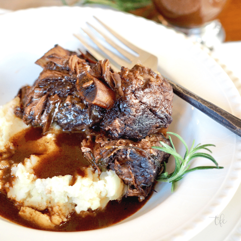 Square image of bowl of juicy Italian braised short ribs over mashed potatoes with rich gravy.