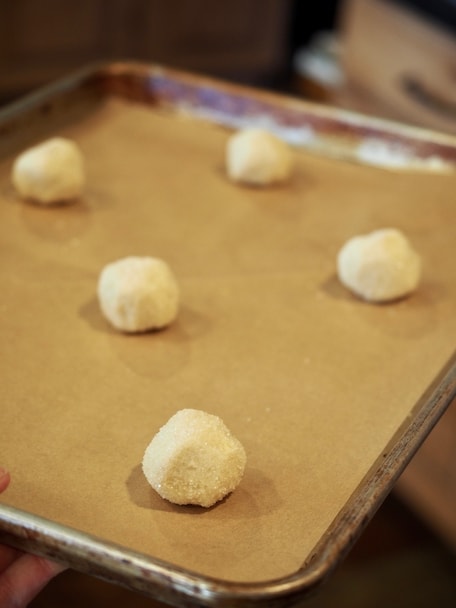 pan banging sugar cookie dough balls on parchment lined baking sheet