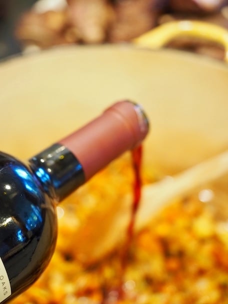 Pouring whole bottle of red wine to deglaze pan for Italian Short Ribs.