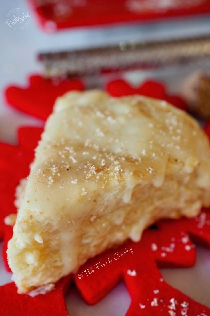 Close up of egg nog scone on red felted wool snowflake with fresh grated nutmeg.