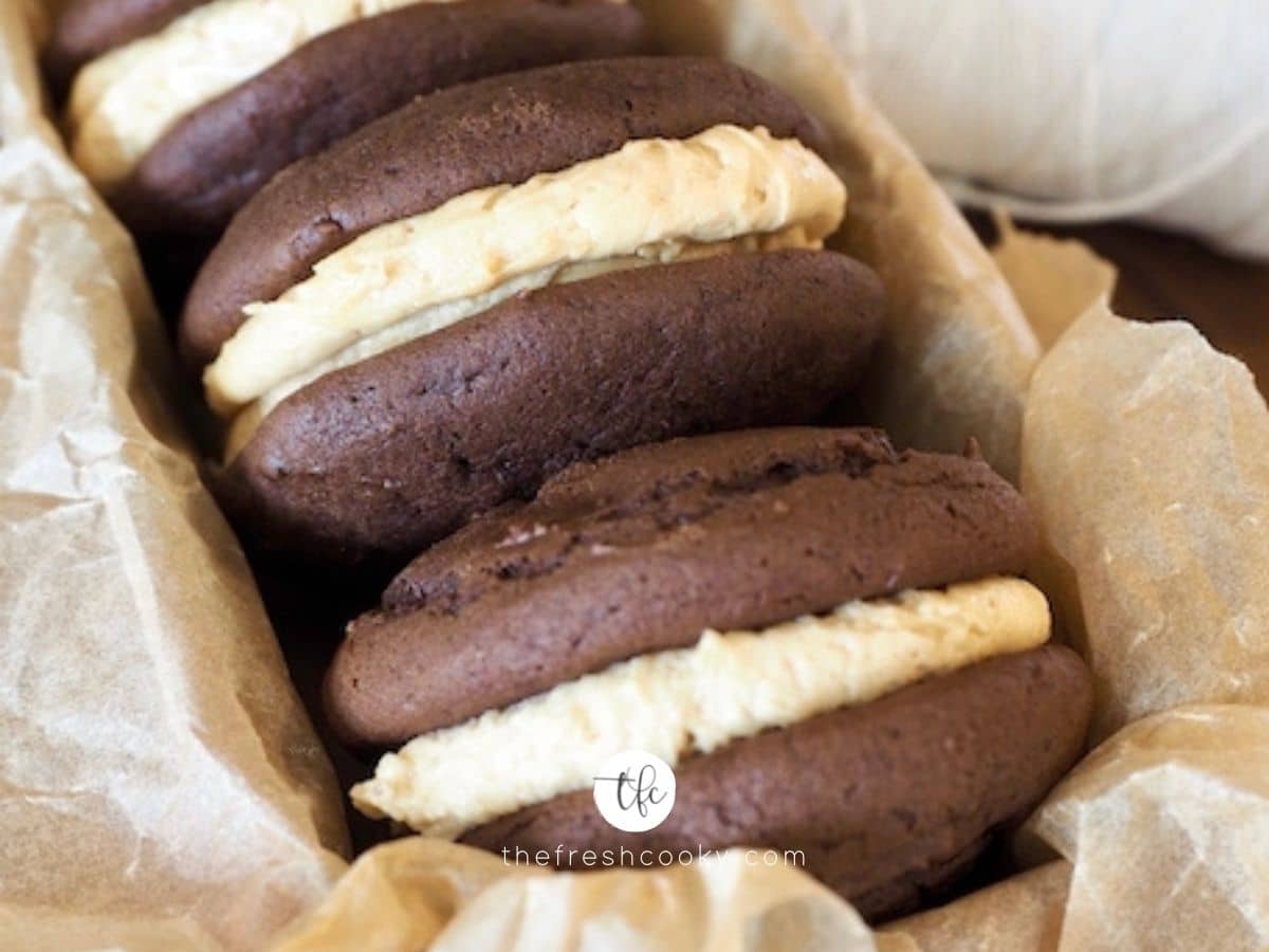 Facebook image with three whoopie pies with fluffernutter frosting stacked in a pan with parchment paper.