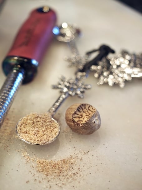 snowflake measuring spoon with fresh grated nutmeg inside, spice Microplane and recently grated whole nutmeg.