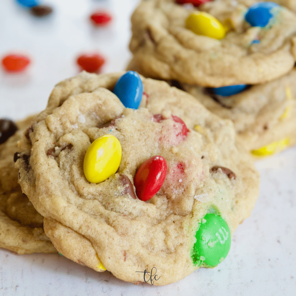 Square image of close up of chewy and soft m & m chocolate chip cookies with a stack behind.