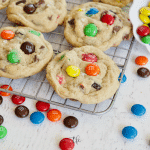 Square image of m & m chocolate cihp cookies on cooling rack with scattered m & m's laying around.