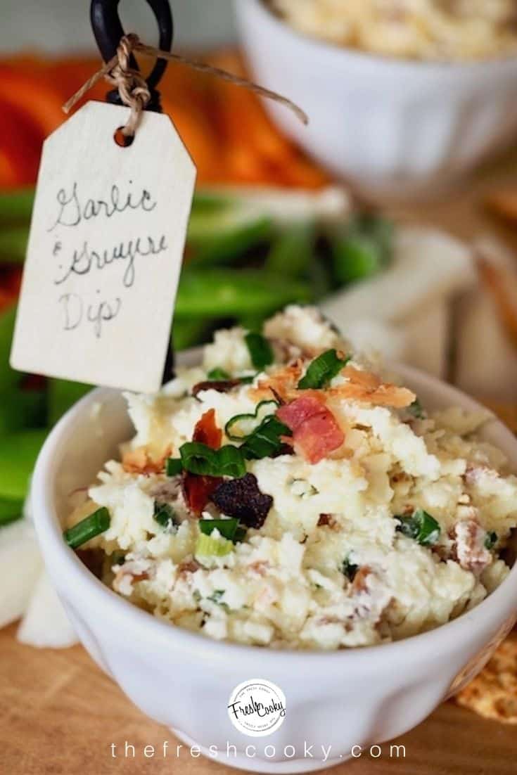 Garlic Gruyere Cheese Dip in white bowl with little tag on naming the dip, with crackers and veggies on a platter. 