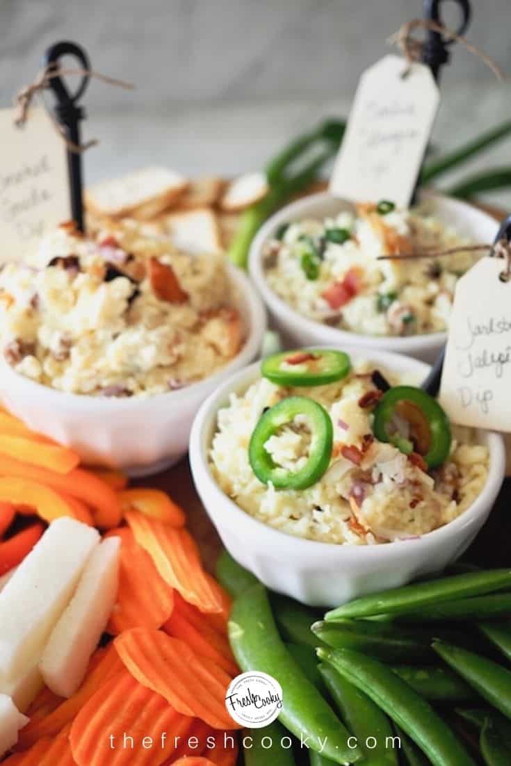 Three different cheese dips in white bowls with veggies surrounding, Jarlsberg Jalapeno, Smoked Gouda and Garlic Gruyere Dip.
