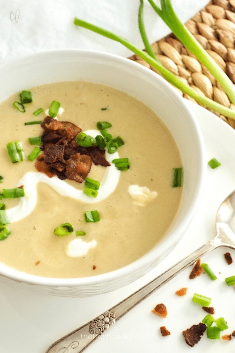 Pin for instant pot potato leek soup with spoon and green onions topped with bacon bits, sour cream and green onions.