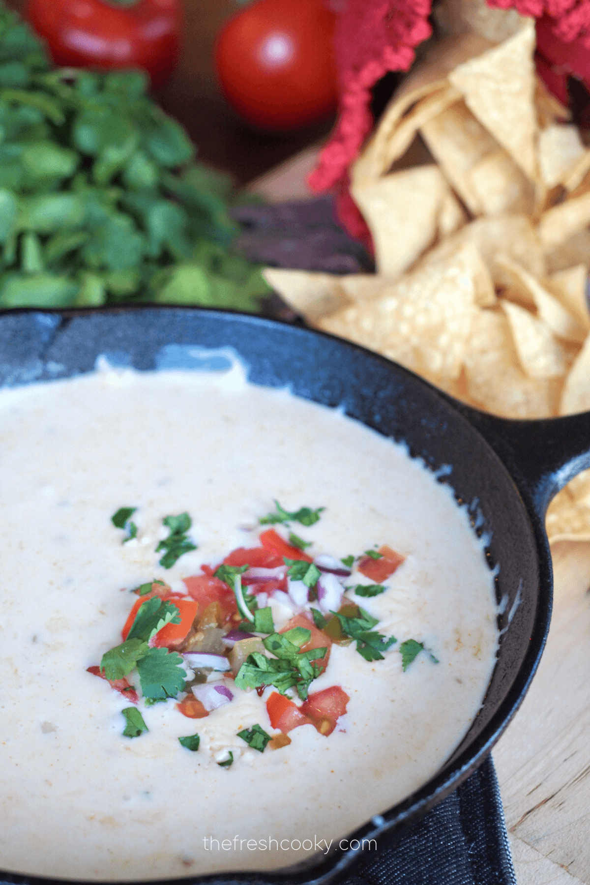 Cast iron pan filled with gooey Mexican White Cheese Dip with tortilla chips and cilantro in background.