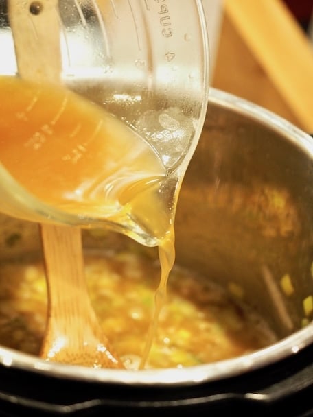 Glass bowl pouring chicken broth into instant pot. 