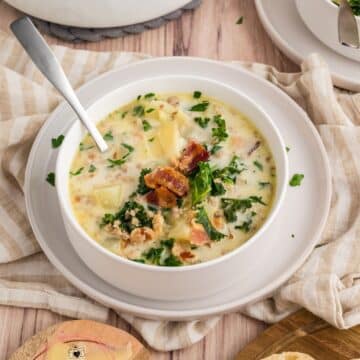 A white bowl filled with creamy and bright Zuppa Toscana, filled with sausage, potatoes, and kale.