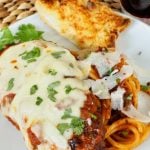 Chicken Parmesan on white plate with spaghetti noodles and slice of garlic toast.