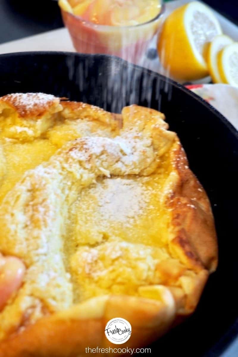 Oven pancake, cooked in a cast iron skillet with lemon in background shaking on powdered sugar