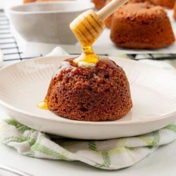 Honey being drizzled on top of a bran muffin with a pat of butter, on a cream plate.