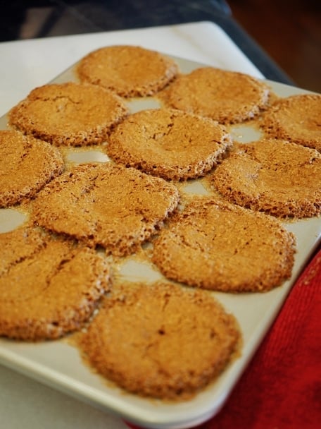 A muffin tin with baked muffins oozing over the tops sitting on a cutting board. 