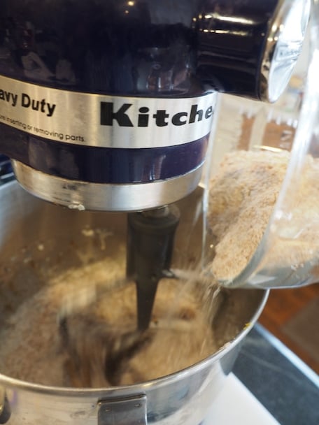 Glass batter bowl pouring in flour mixture into the bowl of a stand mixer (Kitchenaid).