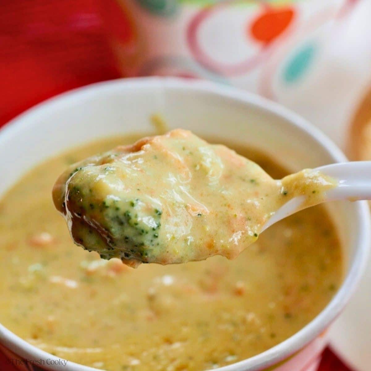 Bowl of broccoli cheese soup with a spoon grabbing a bite, with a chunk of broccoli, carrots, cheese and creamy soup.