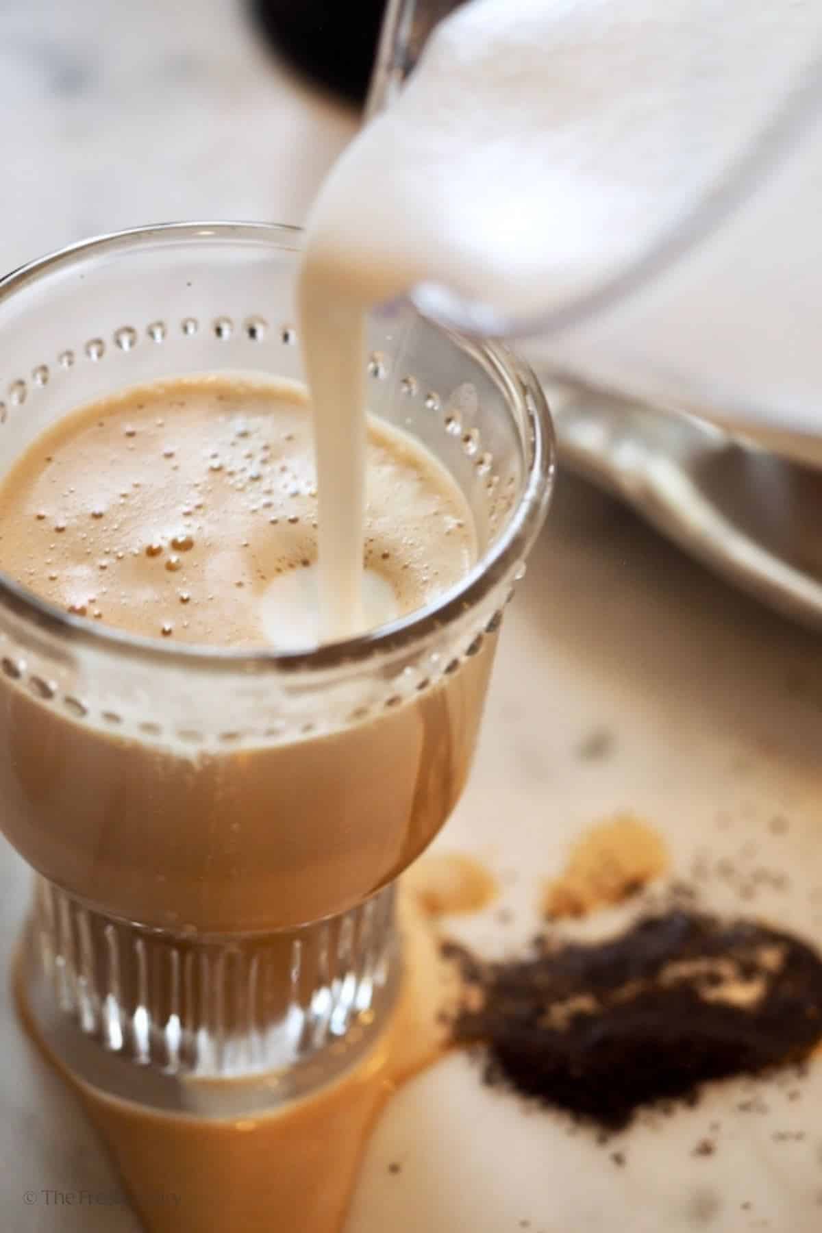 Pouring frothed cream on top of butter coffee. 